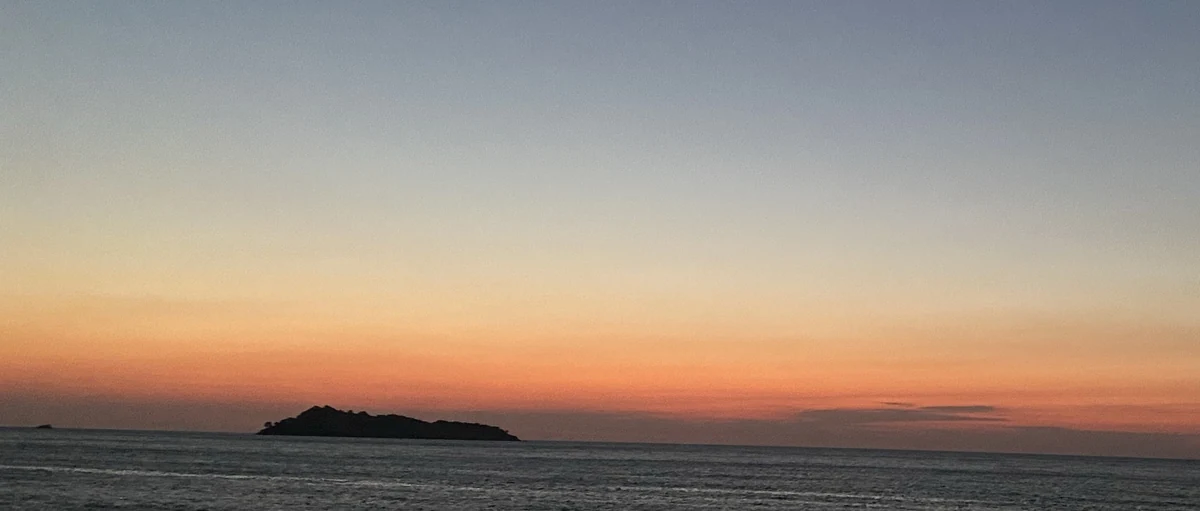 Sunset over the sea from a beach on Lesvos, with a small island dark against the orange horizon.